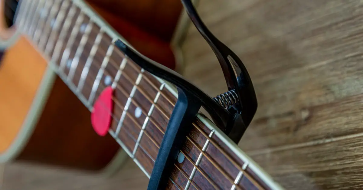 guitar neck with capo on and plectrum sitting in strings