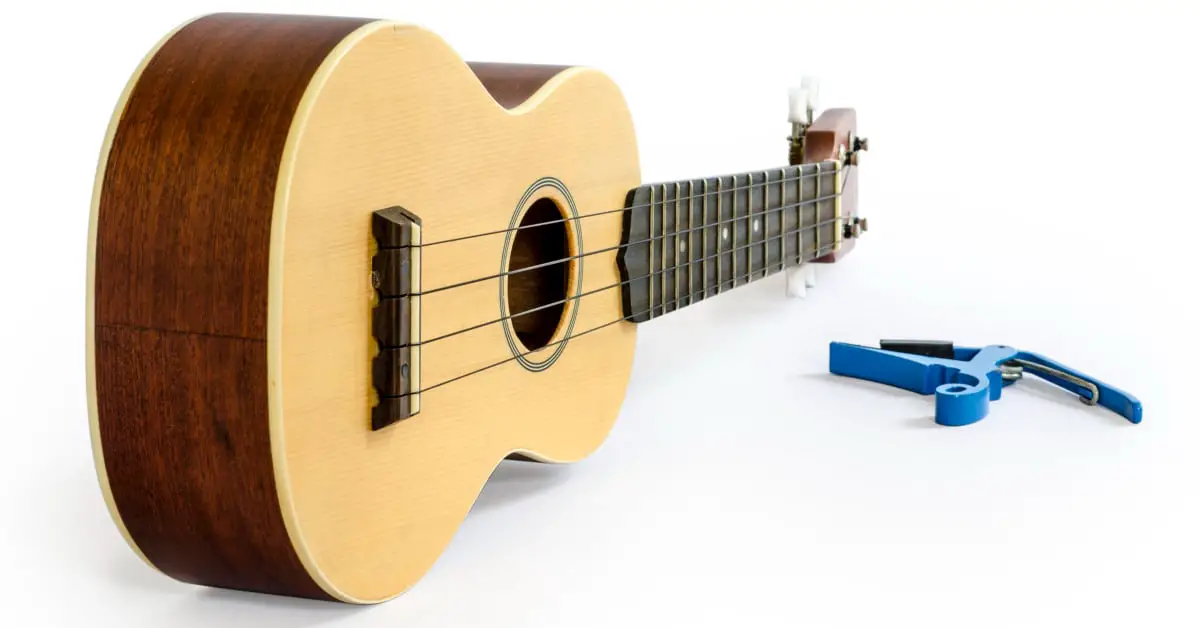 ukulele laying on its side with capo on the ground and white background